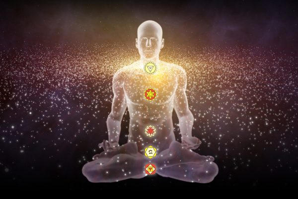 Silhouette in an enlightened Yoga meditation pose with the Hindu Chakras overlapping a galaxy of stars.