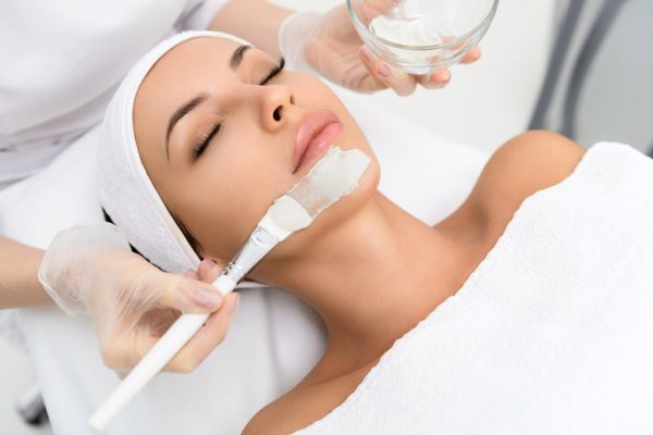 Young girl is enjoying facial procedure at beauty salon. She is lying and getting clay mask with pleasure