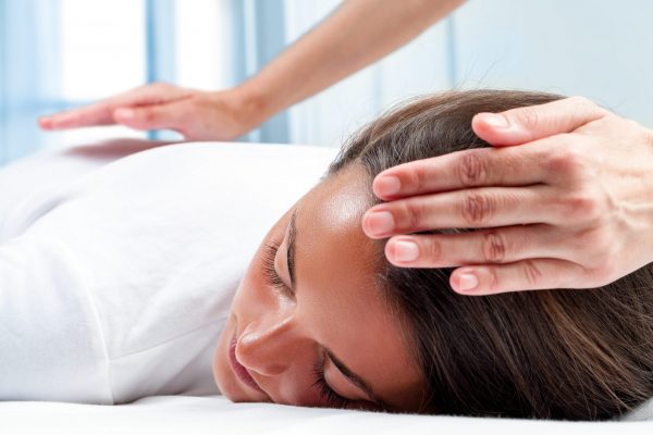 Therapists hands doing reiki therapy on girl. One hand on head and one hand on back.
